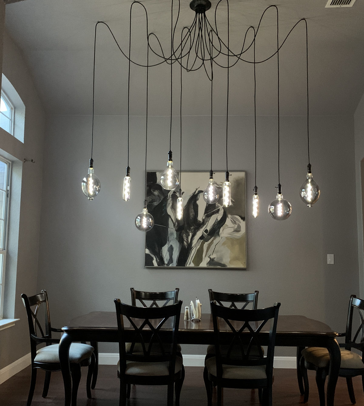 A multi-cord pendant light fixture with large exposed Edison bulbs hung in a swag pattern above a dining table.